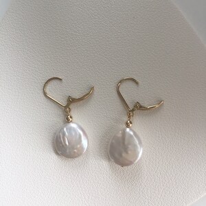 May include: A pair of gold earrings with white pearl drops. The earrings have a simple design and are perfect for everyday wear.
