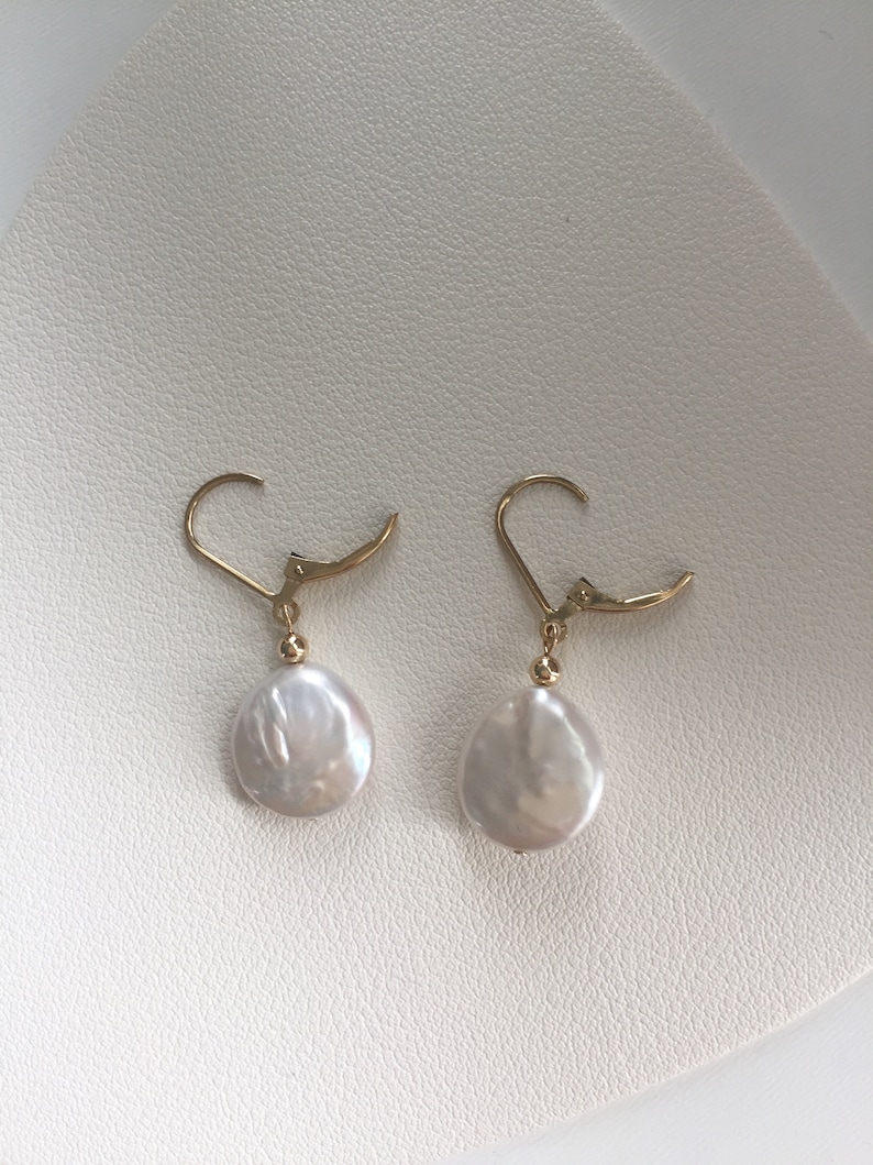 May include: A pair of gold earrings with white pearl drops. The earrings have a simple design and are perfect for everyday wear.