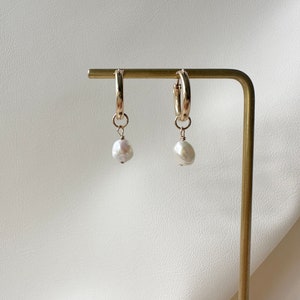 May include: Gold hoop earrings with a single white pearl dangling from each hoop.