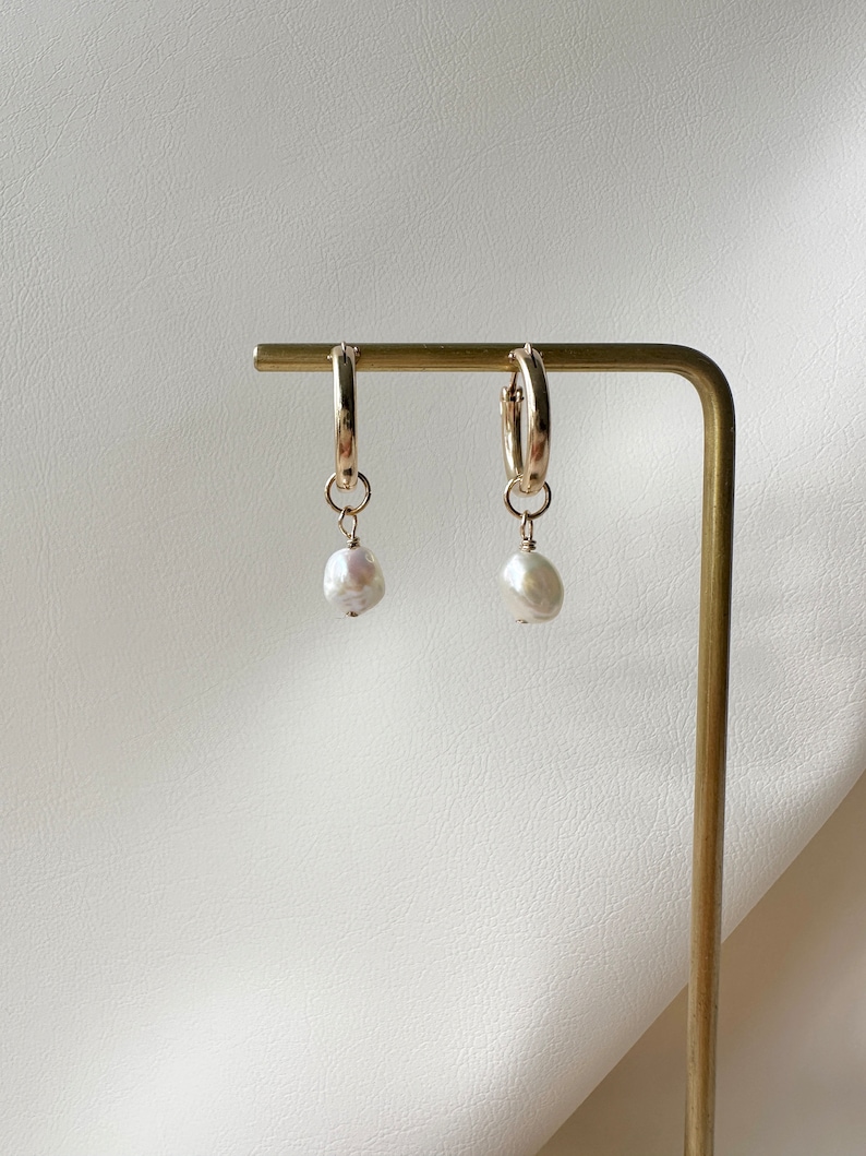 May include: Gold hoop earrings with a single white pearl dangling from each hoop.