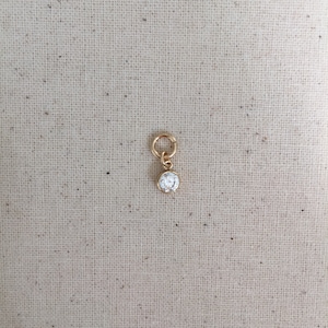 May include: A gold charm with a clear round crystal stone.