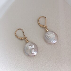 May include: A pair of gold hoop earrings with white pearl dangles. The pearls are round and have a slightly irregular shape.