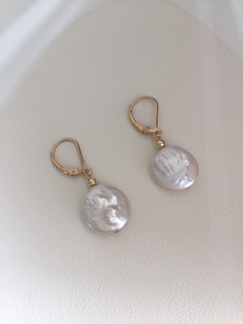 May include: A pair of gold hoop earrings with white pearl dangles. The pearls are round and have a slightly irregular shape.