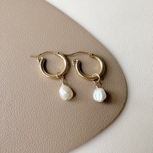 May include: A pair of gold hoop earrings with a single white pearl dangling from each hoop.