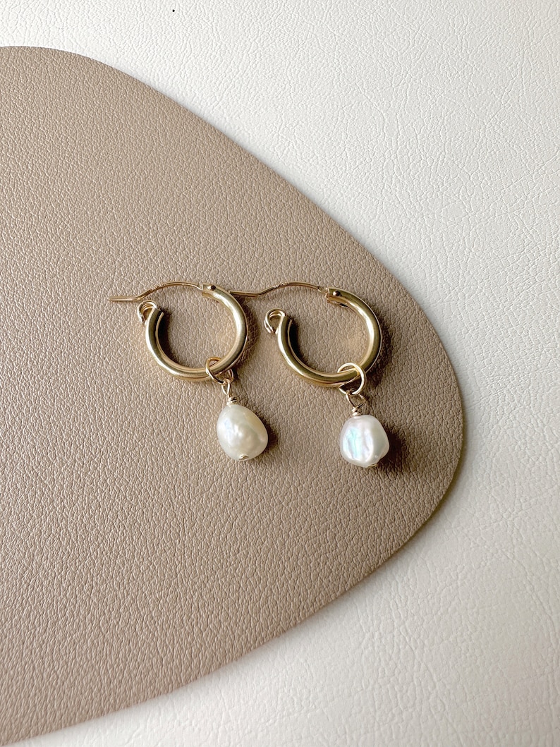 May include: A pair of gold hoop earrings with a single white pearl dangling from each hoop.