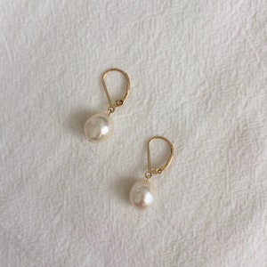 May include: A pair of gold hoop earrings with a single white pearl dangling from each hoop.