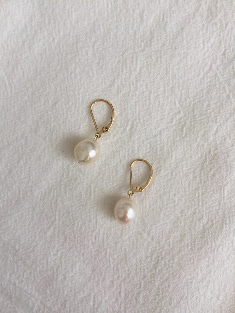 May include: A pair of gold hoop earrings with a single white pearl dangling from each hoop.