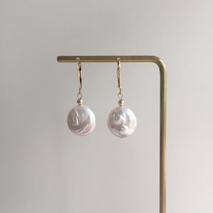 May include: A pair of gold hoop earrings with large, white baroque pearl drops.