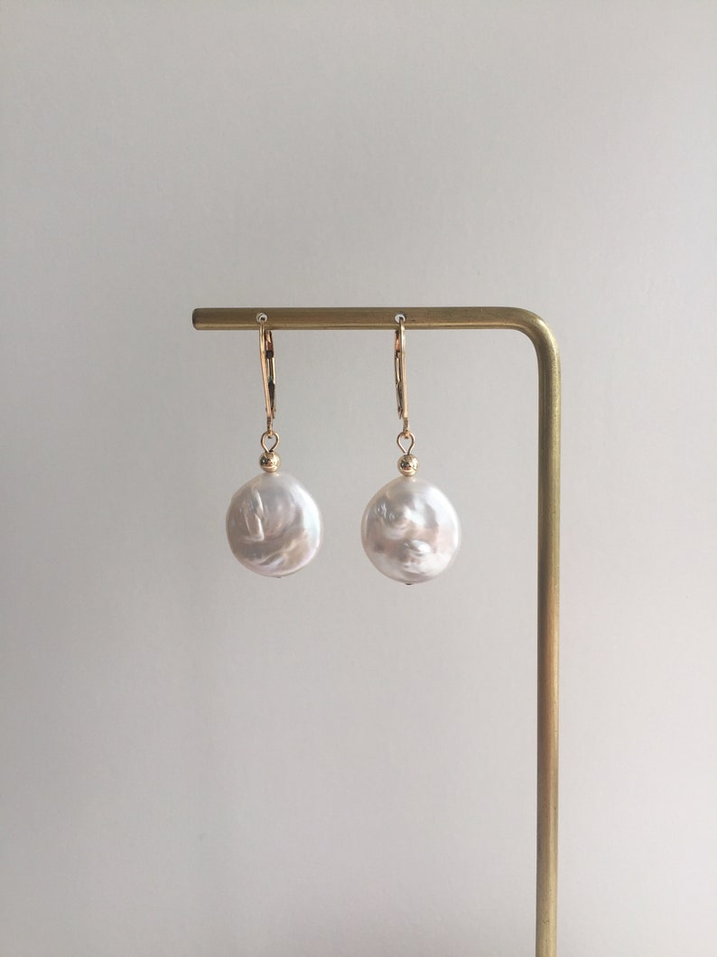 May include: A pair of gold hoop earrings with large, white baroque pearl drops.