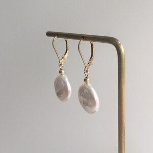 May include: A pair of gold earrings with large, white, irregular shaped pearl drops.