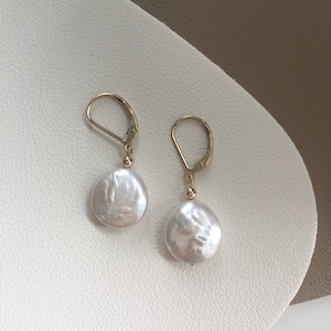 May include: A pair of gold hoop earrings with white pearl drops. The pearls are round and have a slightly irregular shape.
