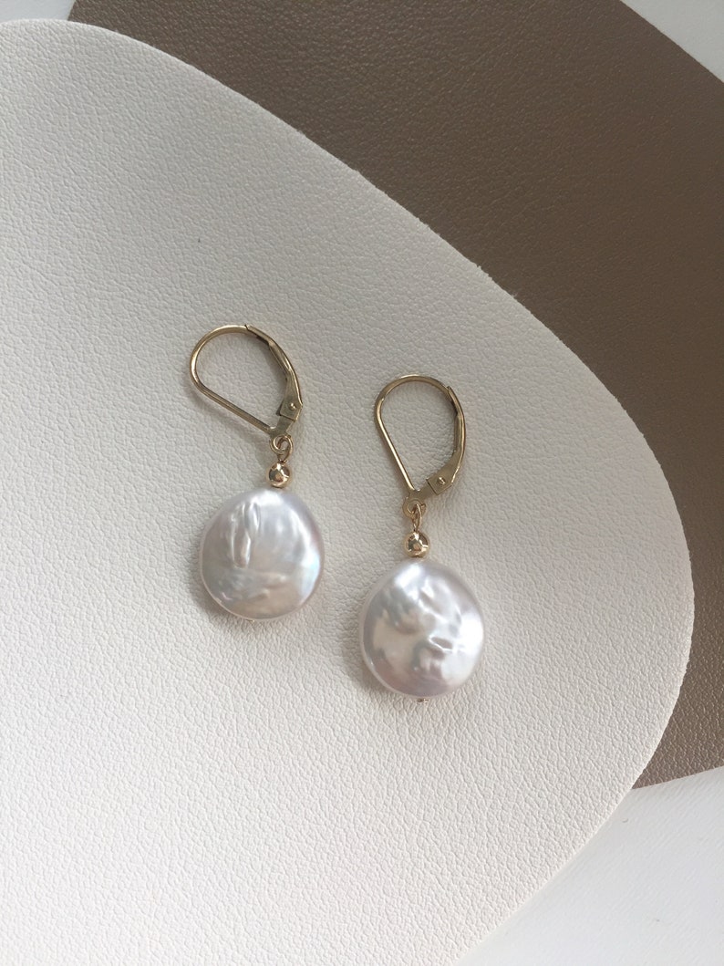 May include: A pair of gold hoop earrings with white pearl drops. The pearls are round and have a slightly irregular shape.