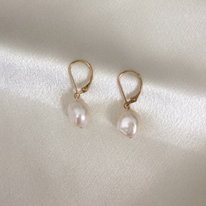 May include: A pair of gold earrings with white pearl drops. The earrings have a simple design and are perfect for everyday wear.