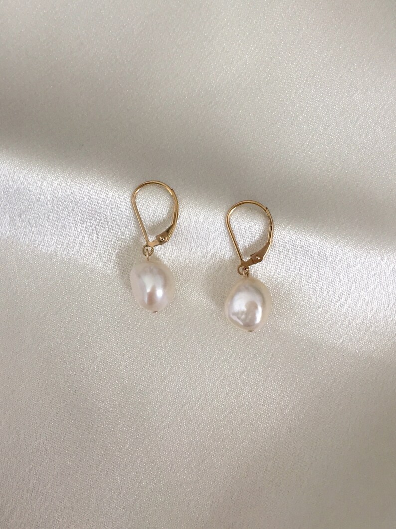 May include: A pair of gold earrings with white pearl drops. The earrings have a simple design and are perfect for everyday wear.