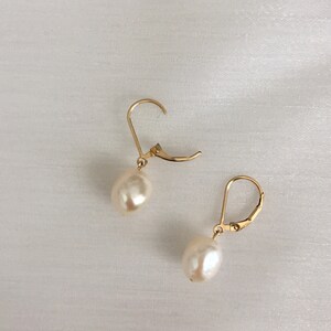 May include: A pair of gold earrings with white pearl drops. The earrings have a simple, elegant design.