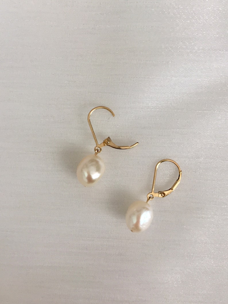 May include: A pair of gold earrings with white pearl drops. The earrings have a simple, elegant design.