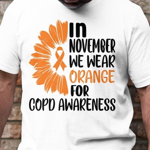 Puede incluir: Camiseta blanca con un diseño de girasol naranja y el texto "En noviembre usamos naranja para la concienciación sobre la EPOC".