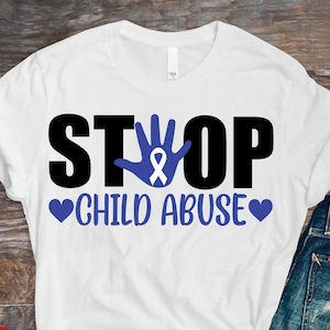 Könnte beinhalten: Weißes T-Shirt mit dem Text "STOP CHILD ABUSE" in schwarzen Buchstaben. Ein blauer Handabdruck mit einem blauen Band befindet sich in der Mitte des Wortes "STOP". Zwei Herzen befinden sich auf beiden Seiten des Textes.
