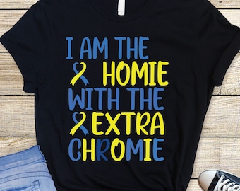Pode incluir: Camiseta preta com o texto "I am the homie with the extra chromie" em letras azuis e amarelas. O texto é rodeado por dois desenhos de fitas amarelas e azuis.