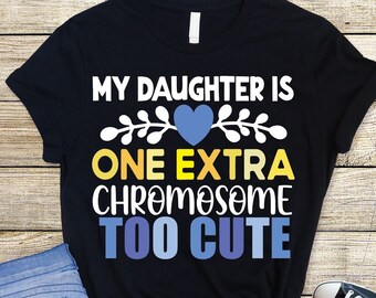 Pode incluir: Camiseta preta com o texto "My daughter is one extra chromosome too cute" em letras amarelas, azuis e brancas. Um coração azul está acima do texto.