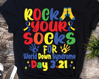 May include: Black t-shirt with the text "Rock Your Socks For World Down Syndrome Day 3.21" in rainbow colors. The text is surrounded by yellow ribbons, handprints, and a pair of yellow socks.