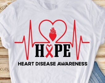Puede incluir: Camiseta blanca con un corazón rojo y una cinta roja, una línea de ECG negra y la palabra "HOPE" en letras negras. El texto "HEART DISEASE AWARENESS" está impreso debajo del diseño.