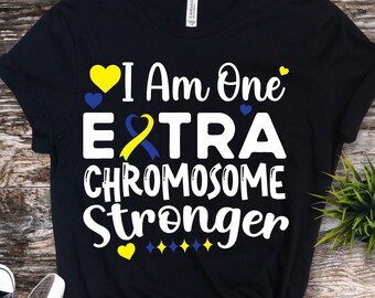 Pode incluir: Camiseta preta com o texto "I Am One EXTRA CHROMOSOME Stronger" em branco, amarelo e azul. O design inclui um coração amarelo, um coração azul e uma fita amarela e azul. A camiseta é combinada com tênis preto e branco.