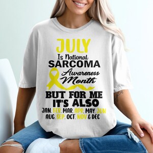May include: White t-shirt with black text that reads "JULY Is National SARCOMA Awareness Month BUT FOR ME IT'S ALSO JAN. FEB. MAR. APR. MAY. JUN AUG. SEP. OCT. NOV & DEC". A yellow ribbon is above the text.