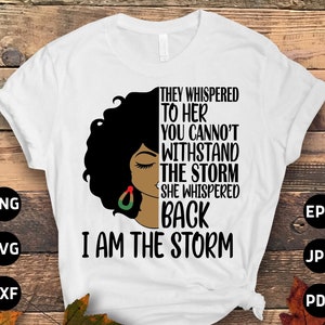 Può includere: Maglietta bianca con un'illustrazione in bianco e nero di una donna con i capelli afro. Il testo "They whispered to her you cannot withstand the storm she whispered back I am the storm" è stampato sulla maglietta.