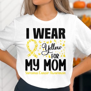 May include: White t-shirt with the text "I WEAR YELLOW FOR MY MOM" in black. A yellow ribbon and butterflies are featured in the design, with "Sarcoma Cancer Awareness" in yellow below the main text.