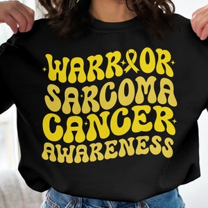 May include: Black sweatshirt with yellow text that reads "Warrior Sarcoma Cancer Awareness" with a yellow ribbon symbol.