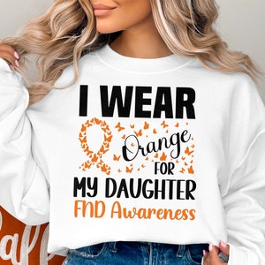 Puede incluir: Sudadera blanca con el texto "I wear orange for my daughter FND Awareness" y una cinta naranja hecha de mariposas.
