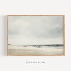 May include: A framed print of a seascape painting. The painting depicts a calm ocean with a sandy beach in the foreground. The sky is a light blue with white clouds.