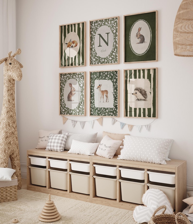 May include: A children's room featuring framed animal art prints, including a fox, rabbit, deer, and hedgehog. The prints are in green and white, with a wooden storage bench below, filled with white bins. Pillows and a giraffe toy complete the decor.