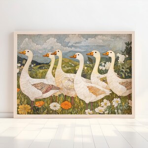 May include: A framed art print featuring six white geese with orange beaks and feet, standing in a field of wildflowers. The background shows rolling green hills, a blue sky, and clouds. The artwork has a vintage, watercolor style.