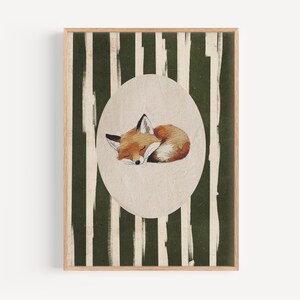 May include: A framed art print featuring a sleeping fox illustration. The fox is depicted in shades of orange, brown, and white, curled up inside an oval shape. The background has vertical green and white stripes.