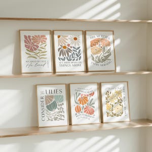 May include: Six framed art prints with floral designs and inspirational quotes. The prints feature various color palettes, including pink, orange, and yellow, with text such as "We loved because He loved" and "Consider the Lilies."