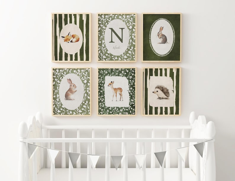 May include: Six framed watercolor prints featuring woodland animals. The prints include a fox, a deer, a rabbit, a hedgehog, and an initial. Each print has a light wood frame and is set against a white background. The prints are above a white crib.