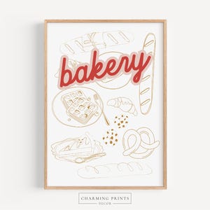 May include: A framed print with a light wood frame featuring a bakery-themed illustration. The word "bakery" is in red and outlined in pink. The illustration includes line drawings of bread, waffles, a croissant, and a pretzel.