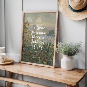 May include: A framed art print with a landscape painting and the text "In Your presence there is fullness of joy." The print is displayed on a wooden bench with a white vase and a straw hat.