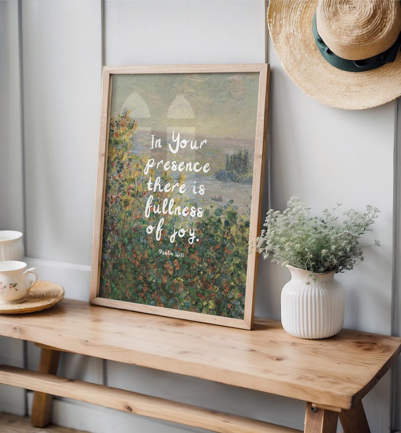 May include: A framed art print with a landscape painting and the text "In Your presence there is fullness of joy." The print is displayed on a wooden bench with a white vase and a straw hat.
