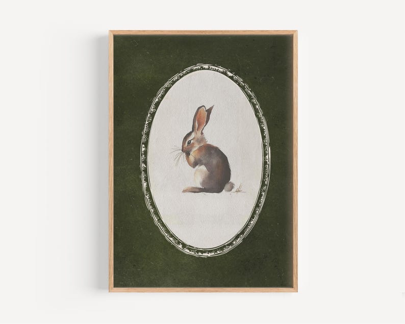 May include: A framed print featuring a watercolor illustration of a brown rabbit within an oval frame. The rabbit is depicted in a seated position against a dark green background. The frame is a light brown color.