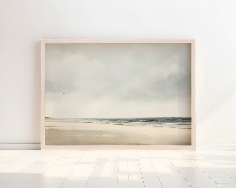 May include: A framed painting of a seascape with a cloudy sky and a sandy beach. The water is a light blue and the sand is a light brown. There are a few birds flying in the sky.