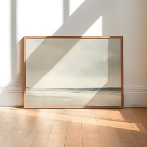 May include: A framed painting of a seascape with a light blue sky, white clouds, and a sandy beach with a calm ocean in the distance.