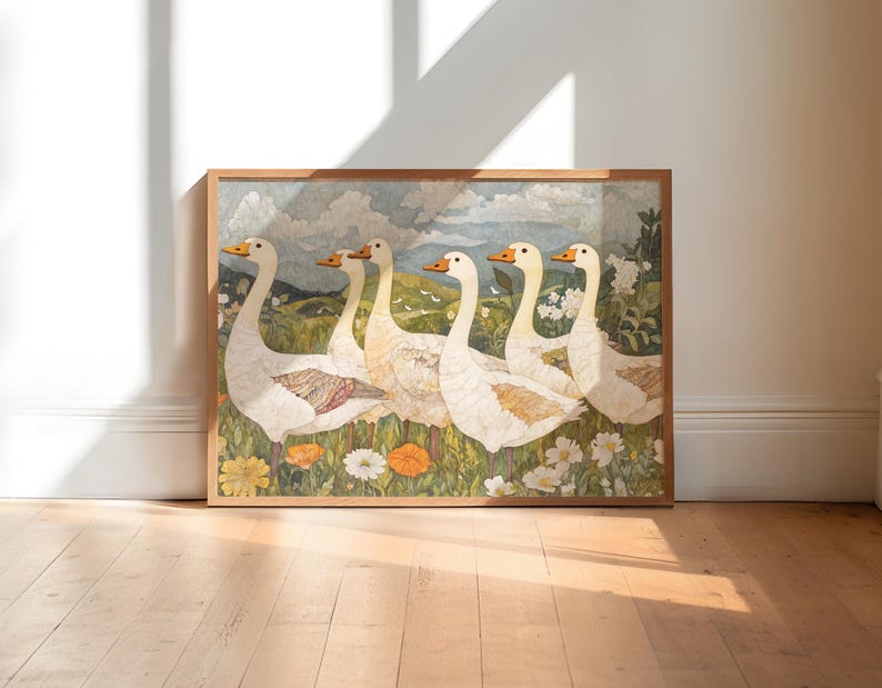 May include: A framed artwork featuring six white geese with orange beaks and feet, set against a backdrop of a green field, flowers, and a cloudy sky. The artwork is in a wooden frame and rests on a wooden floor.