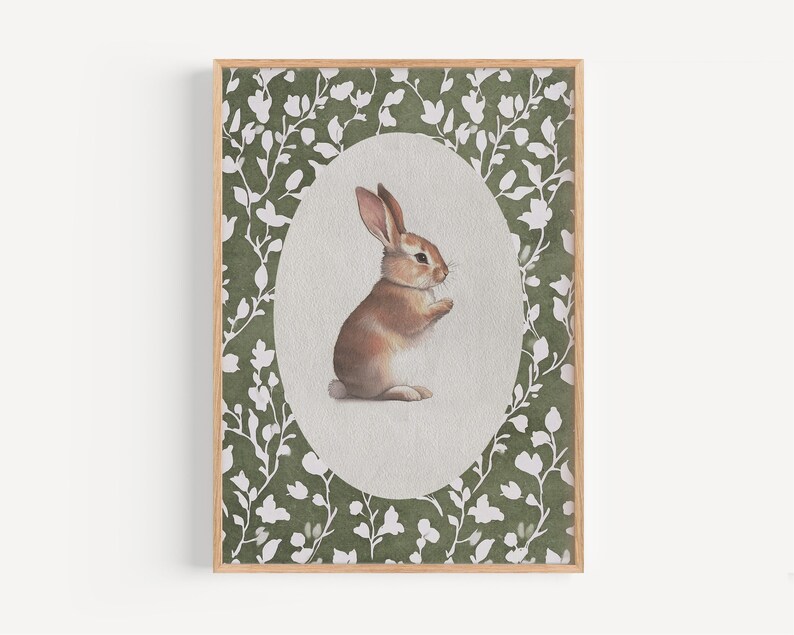 May include: A framed watercolor print of a brown and white rabbit. The rabbit is centered in an oval shape against a light green background. The oval is surrounded by a border of white floral designs, all within a wooden frame.