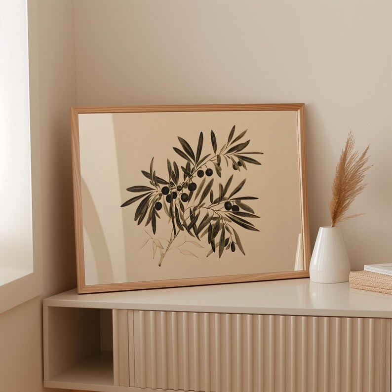 May include: A framed botanical print of an olive branch with black olives. The print is on a cream background and has a light wood frame. The print is hanging on a wall above a light brown cabinet.