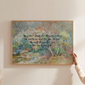 May include: A framed art print featuring a watercolor landscape with a river and trees in shades of green, blue, and brown. The artwork includes a quote from Psalm 42:1-2 in black text. The frame is made of light-colored wood.
