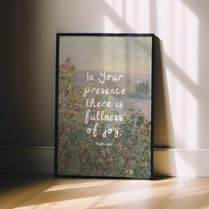 May include: Framed art print featuring a landscape painting with a quote: "In Your presence there is fullness of joy." The artwork has a black frame and is leaning against a wall. The quote is in white script.