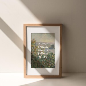 May include: Framed art print featuring a landscape painting with the text "In Your presence there is fullness of joy." The artwork is set in a light brown wooden frame with a white mat. The print has a soft, natural color palette.